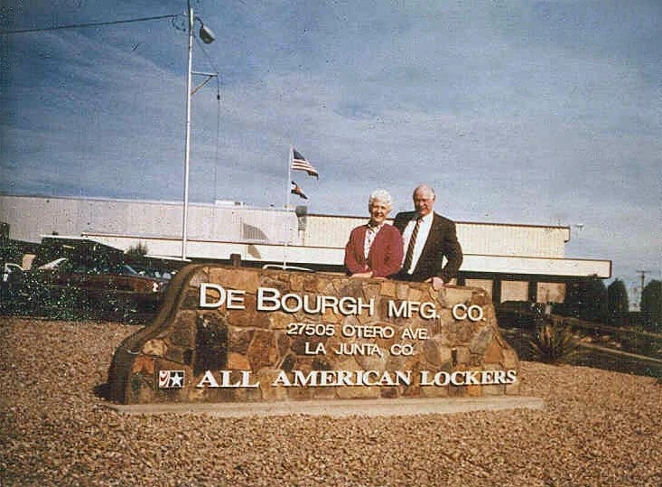 woman and man standing behind a De Bourgh Mfg. sign at company headquarters