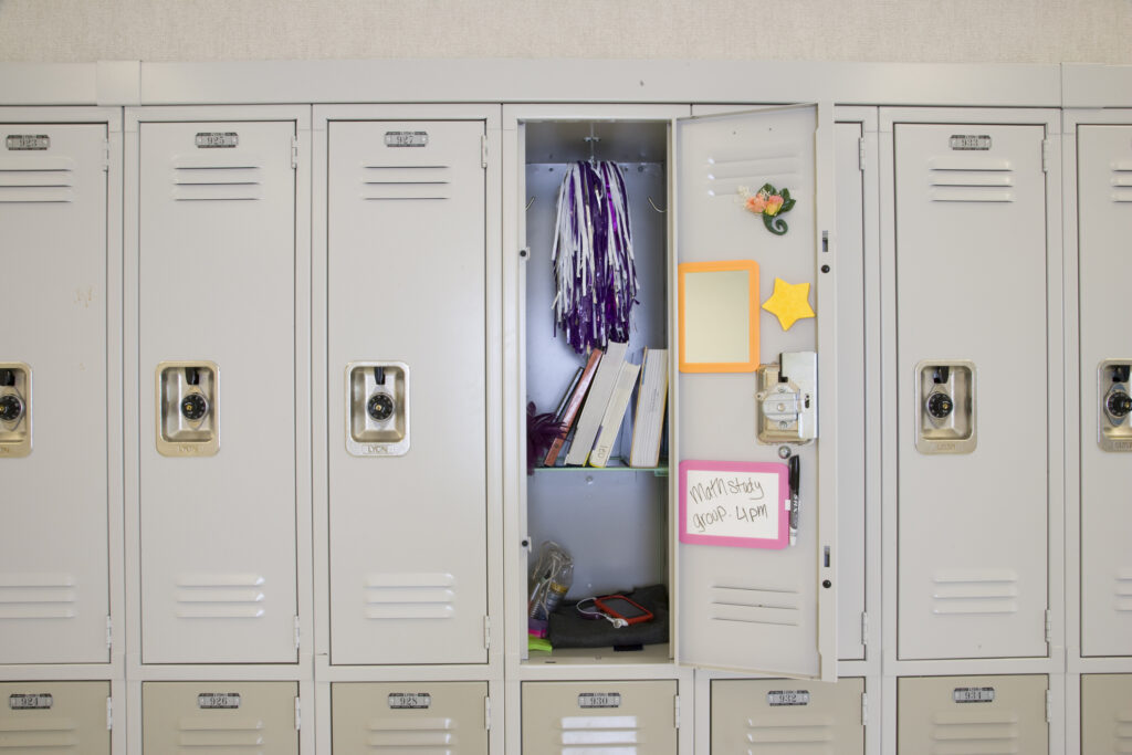 open junior high locker with mirror, books and cheerleading pom poms inside