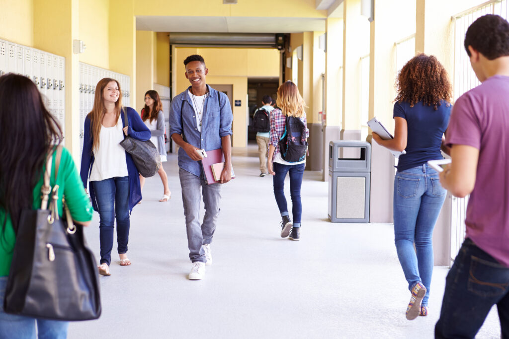 Group Of High School Students Smiling and Walking Along School Hallway